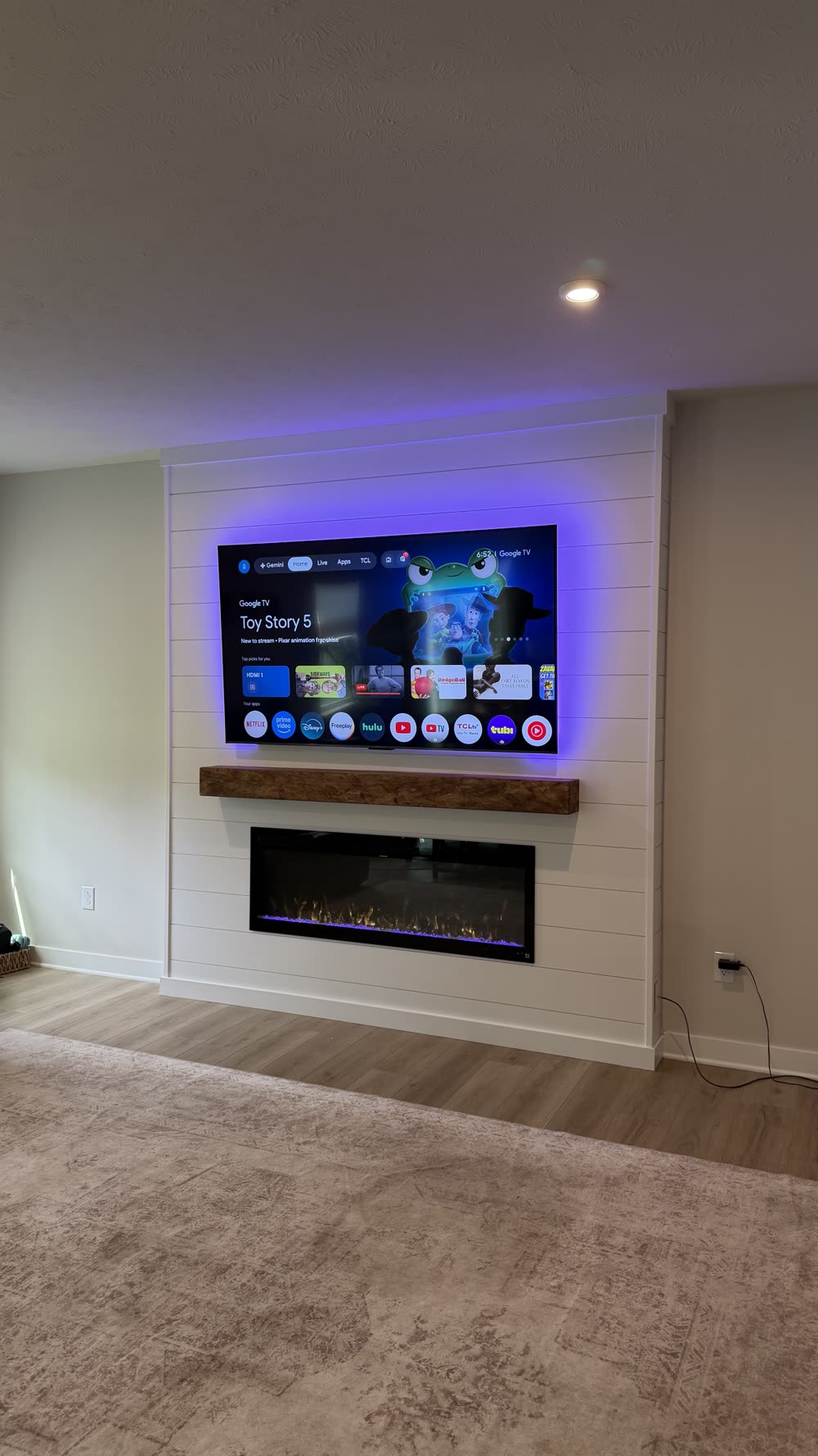 White shiplap media wall with TV on, floating mantel, and lit fireplace