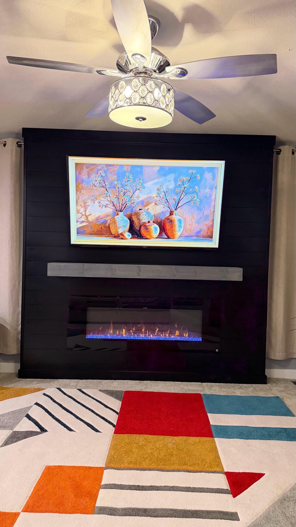 Black horizontal shiplap wall with TV, gray floating mantel, and blue flame fireplace