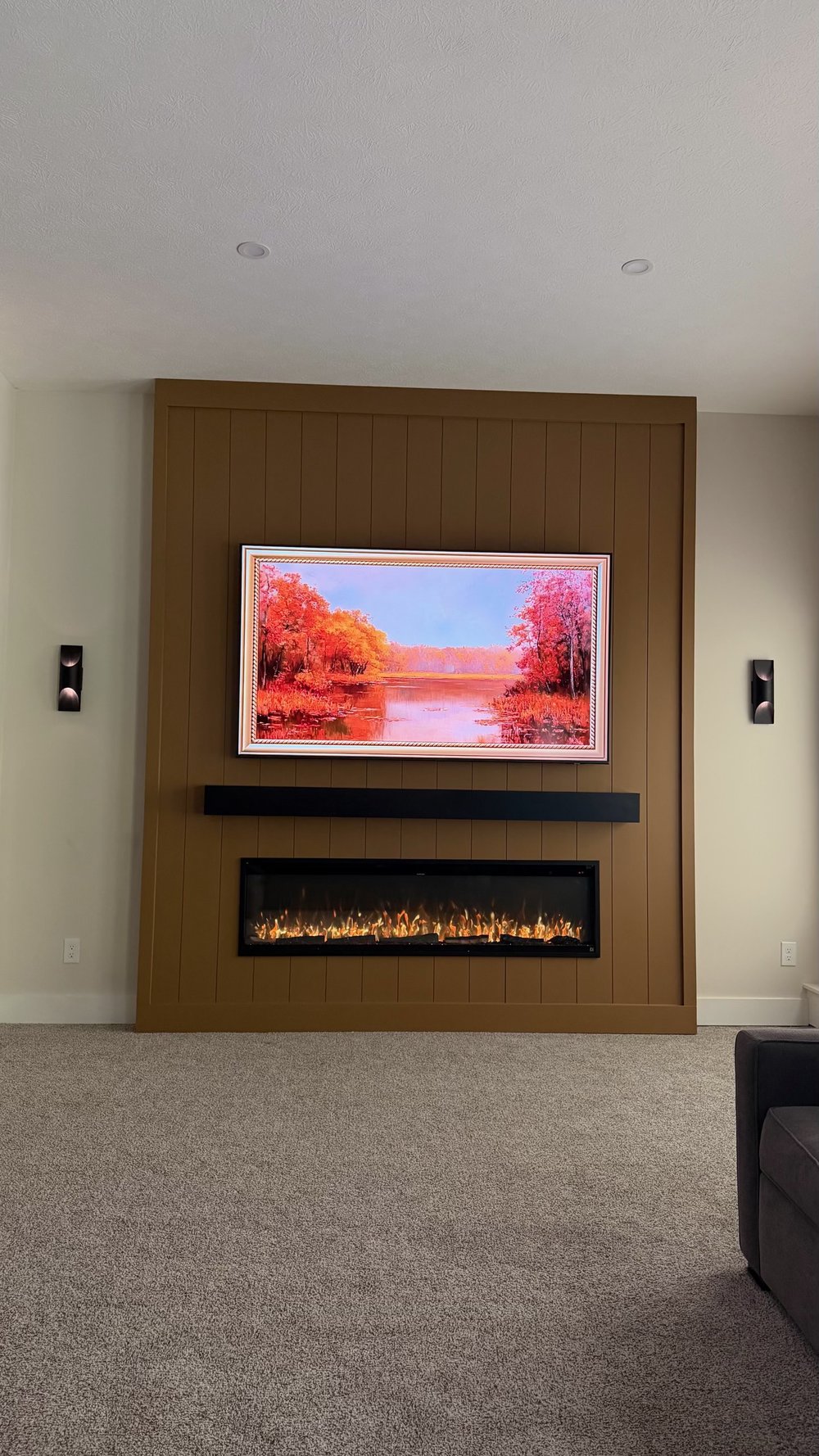 Caramel-painted vertical slat media wall with TV, black floating mantel, fireplace, and black wall sconces
