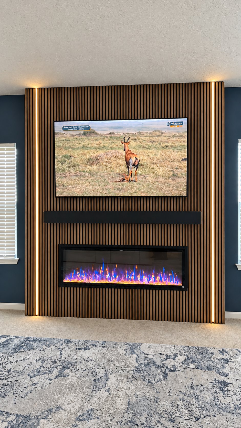 Vertical slat wall with LED edge lighting, mounted TV, and blue flame fireplace against a navy wall