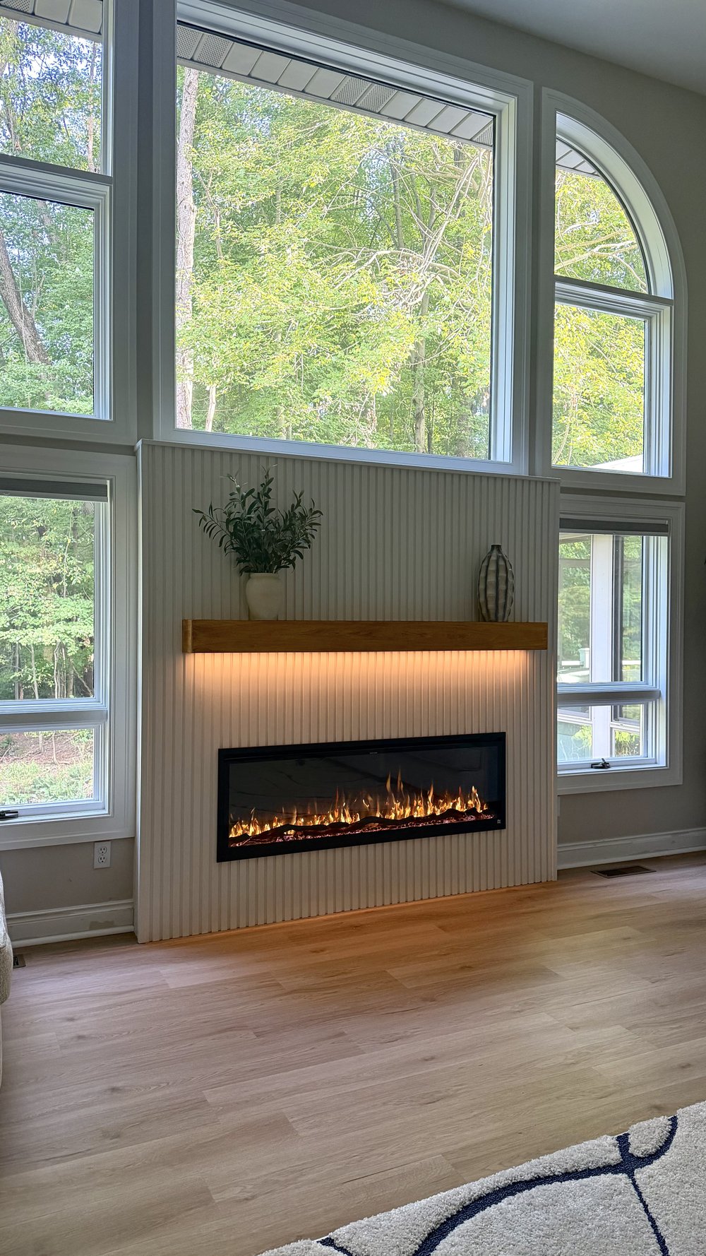 White vertical panel fireplace wall with wood mantel and under-mantel LED glow in a sunlit room, no TV